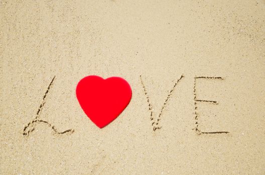 Sign "Love" with red heart shape on the sandy beach