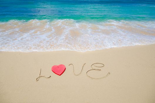 Word "Love" with red heart shape on the sandy beach