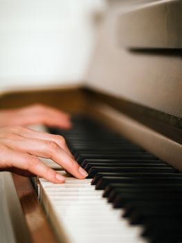 Photo of female hands playing an upright piano. Very shallow depth of field with focus on fingers.
