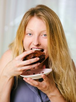 Photo of a beautiful blond woman in her early thirties with log blond hair eating a large piece of brownie or cake.