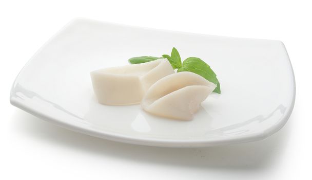 Two raw rings of squid with green basil leaves on the white plate