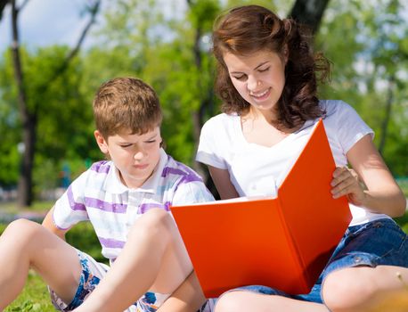 boy and a woman in a summer park reading a book together