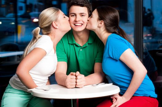 Two attractive girls kissing handsome young boy in a restaurant.