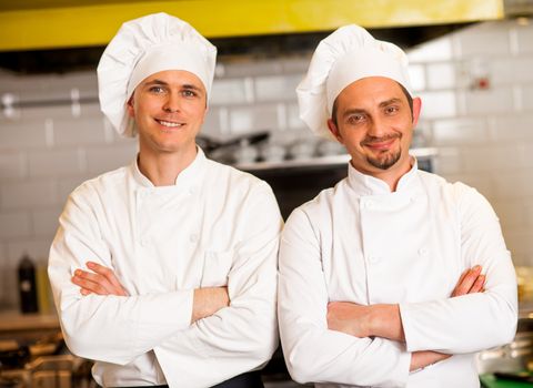 Two smart and confident smiling male chefs posing with arms crossed.