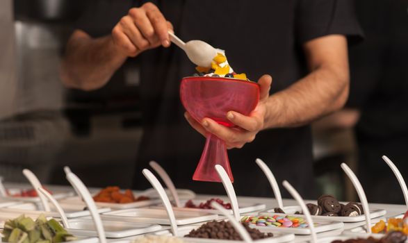 Cropped image of a man decorating ice-cream with gems and jellies.