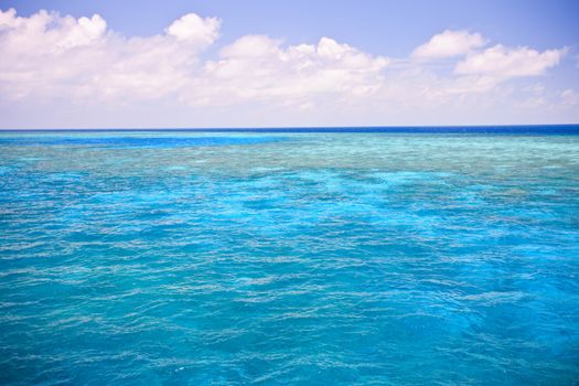 Background image of an azure blue ocean with shallow submerged offshore reef under a cloudy blue summer sky