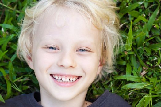 A very cute happy smiling boy lying in the grass looking at camera.