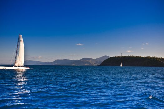 View across a calm blue ocean of a small catamaran sailing off the Australian coast