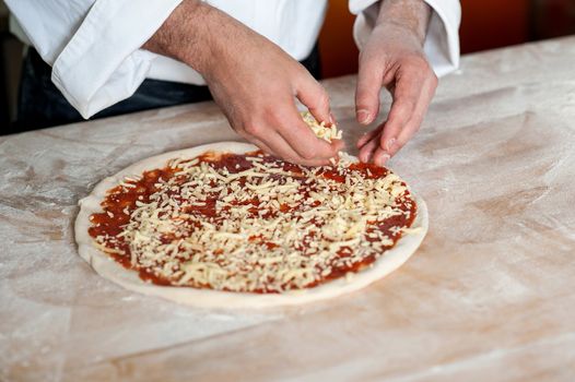 Chef spreading cheese toppings on pizza base