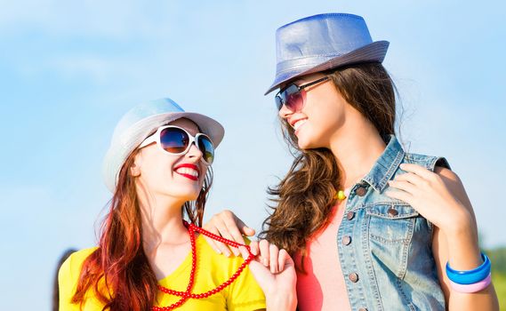 Two young girlfriends having fun on the background of blue sky and friends