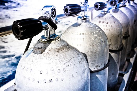 Line of compressed air tanks on a scuba diving boat staning on deck alongside the railing as the boat speeds through the ocean to the dive site