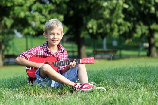 happy boy sitting on grass and play guitar