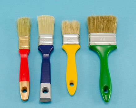 different colors and size hand paint brushes on blue background.