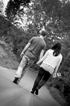 Young happy couple enjoying each others company outdoors walking down an empty road in black and white.