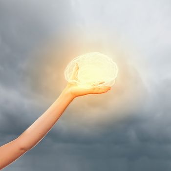 Close-up image of human hand holding brain illustration