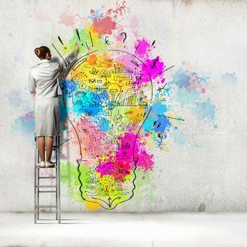 Back view of businesswoman drawing colorful business ideas on wall