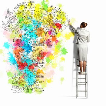 Back view of businesswoman drawing colorful business ideas on wall