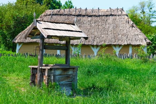 Old village well with a wood roof with a house on background