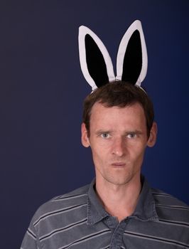 Angry man of motley with rabbit ears on dark background
