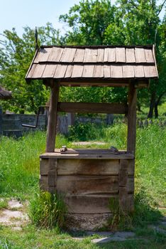 Old village well with a wood roof with green garden on background