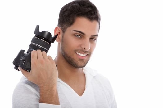 Handsome young photographer holding a camera in his hand above his shoulder smiling at the camera isolated on white