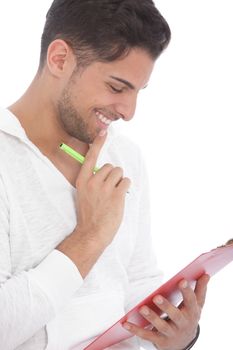 Handsome young man smiling as he reads notes on a clipboard standing with his hand to his chin, isolated on white