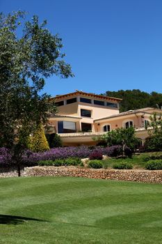 Manicured lush green lawns surrounded by a flowering garden below a clubhouse or modern house