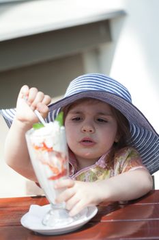 little girl eats ice cream from a tall glass