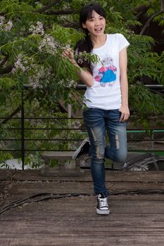 Asian girl standing amongst leaves by tree