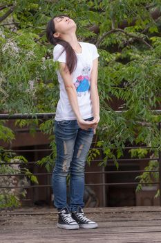 Asian girl standing amongst leaves by tree