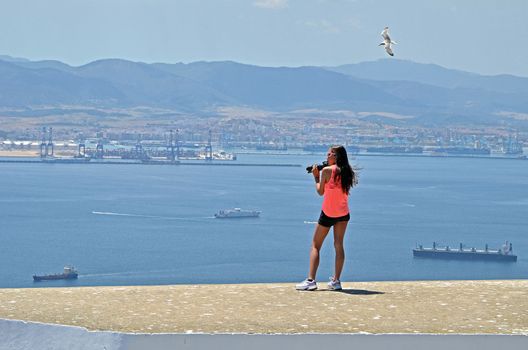 A teenage girl standing on a wall in Gibraltar with a DSLR and telephoto lens.