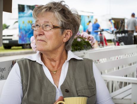 Retired pensioner woman sitting alone in an outdoor cafe