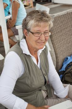 Happy retired pensioner woman sitting alone in an outdoor cafe