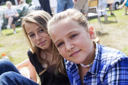 two teenagers sitting on a lawn at a market in Sweden, looking at camera