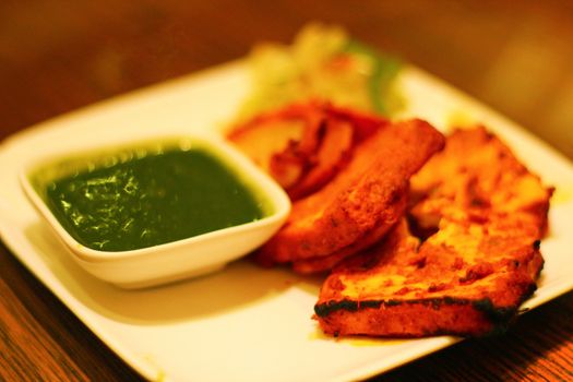 Paneer cheese grilled in the tandoor with coriander and green chili sause in a restaurant in Mumbai, India. Paneer is a popular vegetarian substitute for meat.