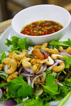 Green thai-style salad with mixed vegetables, smoked fish and cashew nuts in a restaurant in Bangkok, Thailand