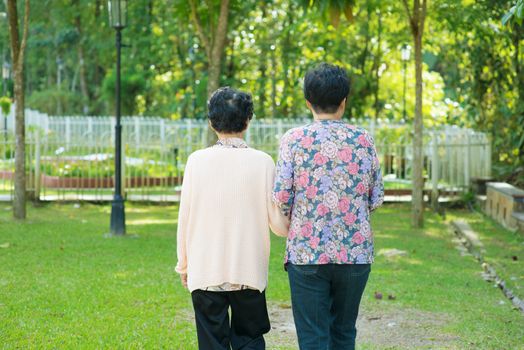 Rear view of Asian 80s old mother and 60s senior daughter holding hands walking at outdoor park.