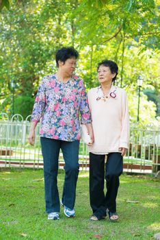 Asian 80s old mother and 60s senior daughter holding hands walking at outdoor park.