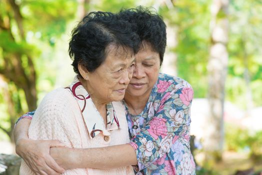 Candid shot of an Asian mature woman hugs and consoling her crying old mother at outdoor natural park. 