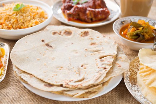 Chapatti roti, curry chicken, biryani rice, salad, masala milk tea and papadom. Indian food on dining table.