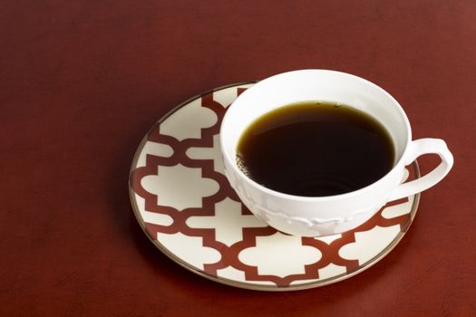 A stylish coffe cup and saucer set on a red table.