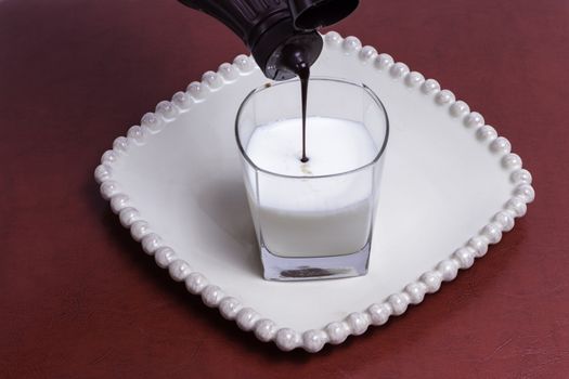 Chocolate syrup being added to a fresh glass of milk.