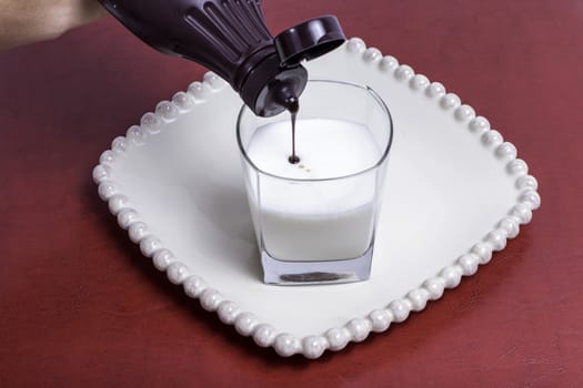 Chocolate syrup being added to a fresh glass of milk.