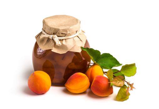 Apricot jam in a glass jar with ripe bright apricots with leaves on a white background