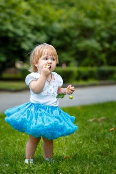 Little blond girl in a blue skirt eating an apple