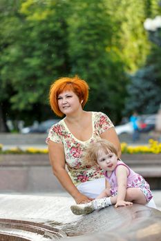 Family, mother and daughter are sitting on the edge of a fountain in a city park