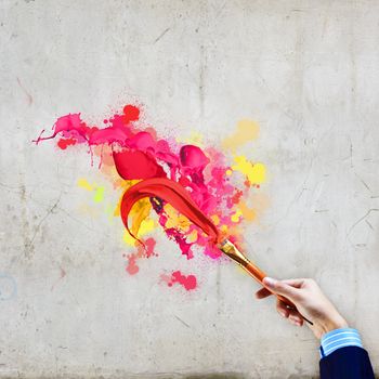 Close-up of human hand holding paint brush making colorful paint splashes