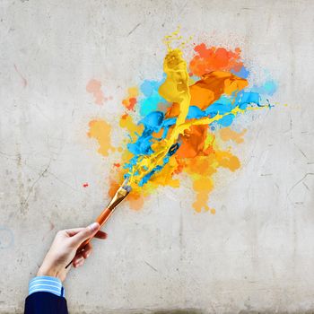 Close-up of human hand holding paint brush making colorful paint splashes