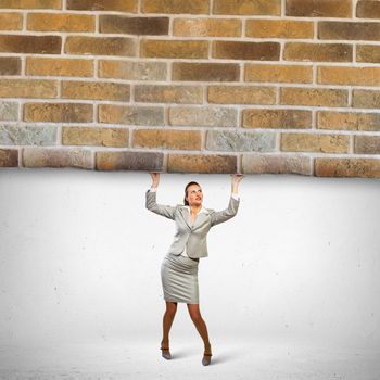 Image of businesswoman lifting brick wall above head