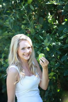 Young woman holding a green apple in her hand standing in front of a leafy green bush